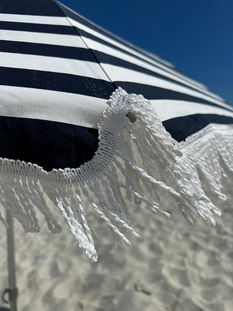 Hollie & Harrie Classic Fringe 210cm cotton beach umbrella with navy and white stripes and white fringe against a blue sky