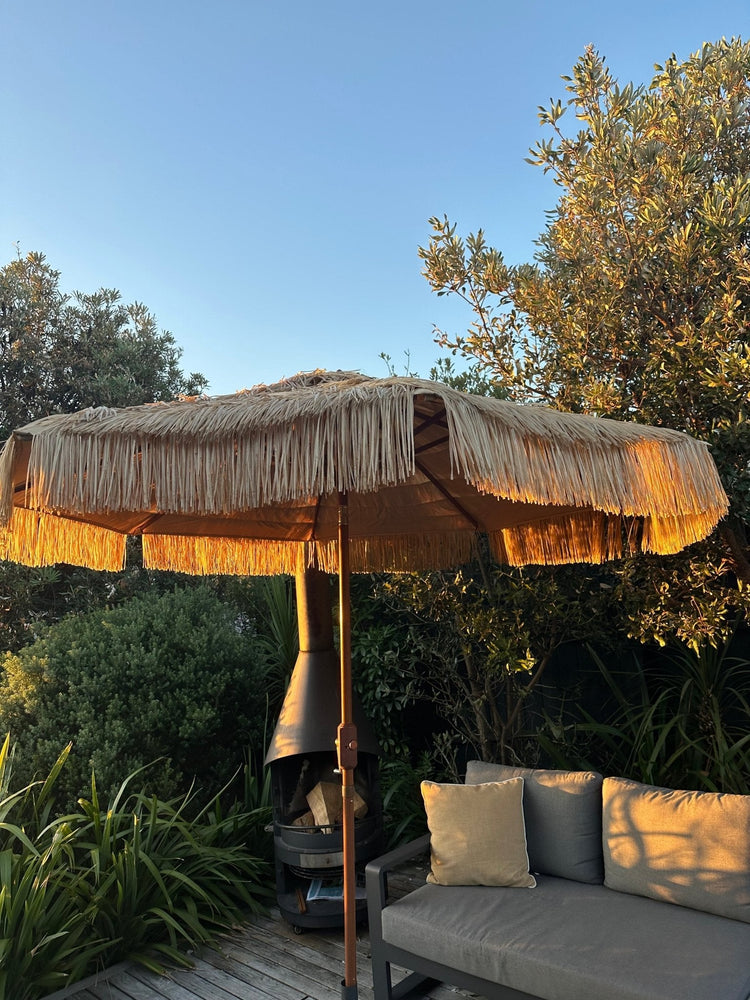 Hula 275cm Market Umbrella with raffia thatch canopy and crank lift system on outdoor patio at sunset