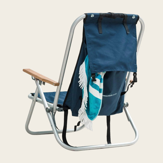 Beachkit Wearever Backpack Chair with aluminum frame, backpack design, wooden arms, and blue fabric seat with towel hanging.