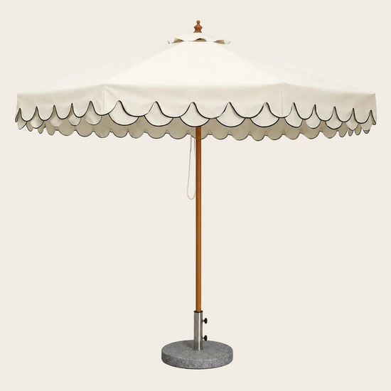 An outdoor patio umbrella with a cream-colored canopy featuring a scalloped edge, a natural wood pole, and a round gray concrete base on a white background.