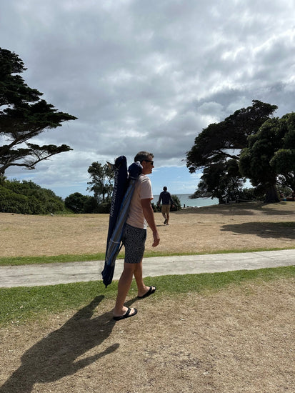 Man carrying folded navy Beachkit’s Ultimate Beach Cabana on shoulder in park setting